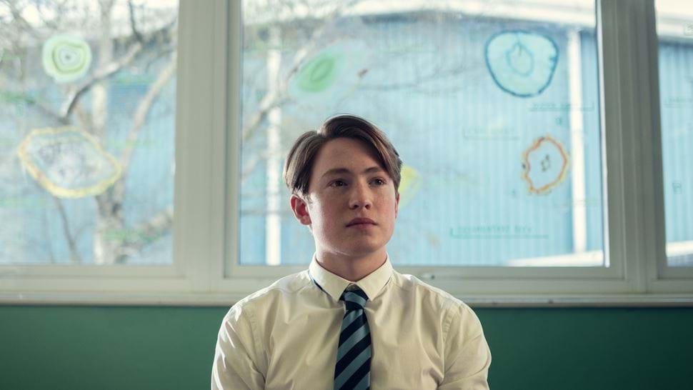 A boy sitting in his classroom, a still from Heartstopper.